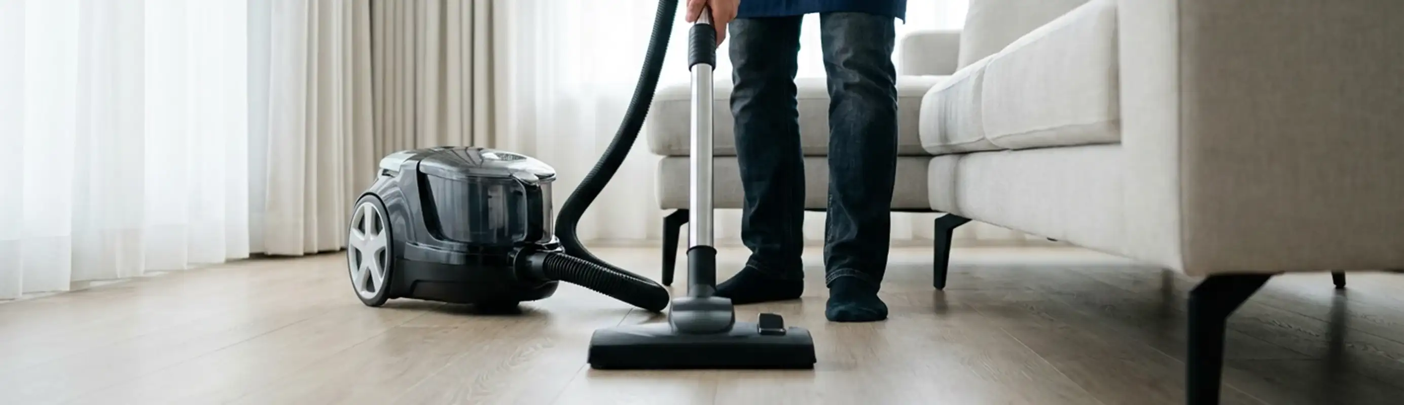 Professional house cleaner vacuuming a living room floor with a canister vacuum cleaner, Overland Park, KS.
