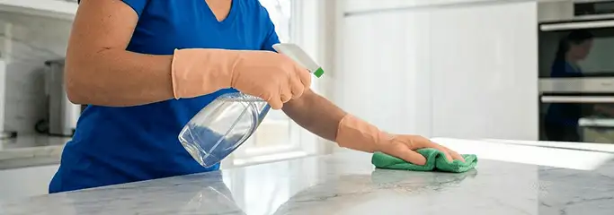 Maid service worker spraying and wiping a kitchen countertop with a microfiber cloth for sanitizing, Overland Park, KS.