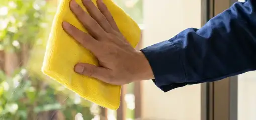 House cleaner wiping a glass window with a yellow microfiber cloth for streak-free cleaning, Overland Park, KS.